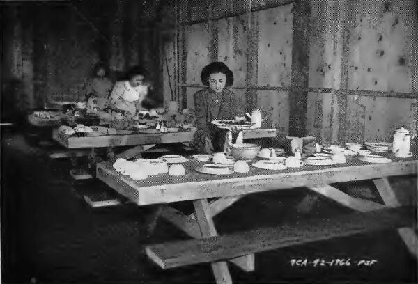 Evacuee waitresses setting tables in a mess hall in one of the assembly centers