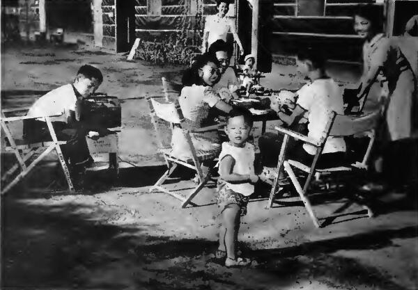 A family group enjoy a card game and the radio outside of their quarters at Assembly Center